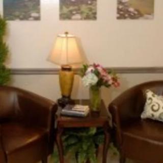 A cozy lobby area with two leather chairs, a small table with a lamp, and a vase of flowers.