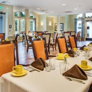 A well-arranged dining room with tables set for guests, featuring yellow cups and brown napkins.