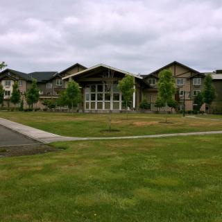 A large building with a modern architectural design surrounded by a grassy lawn and trees under a cloudy sky.
