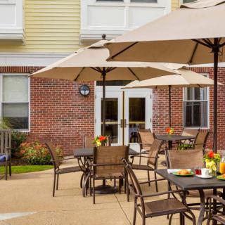An inviting outdoor patio area with tables, chairs, and umbrellas in front of a brick building.