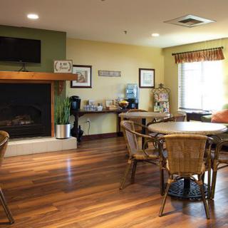 A cozy seating area with wooden flooring, featuring a fireplace and several tables and chairs.