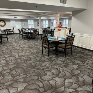 An empty dining area with multiple tables and chairs on a patterned carpet.