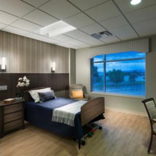 A modern hospital room with a single bed, nightstand, and large window.