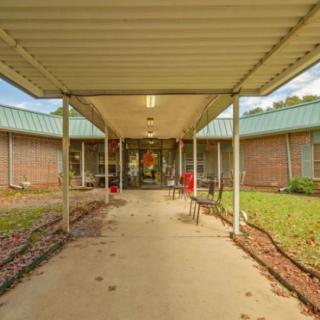 A covered walkway leads to the entrance of a brick building surrounded by landscaped grounds.