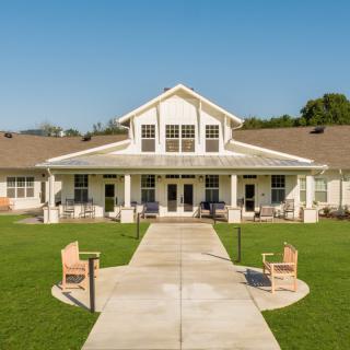 A picturesque view of a house with a spacious lawn and benches.