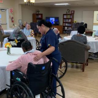 A caregiver assisting an elderly person in a wheelchair within a nursing home setting.