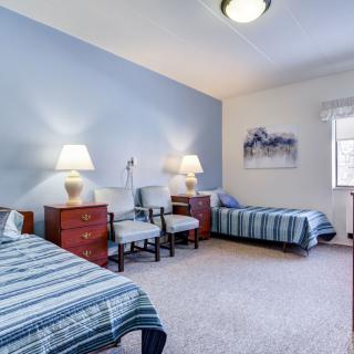 A cozy bedroom with two single beds, nightstands, lamps, and seating.