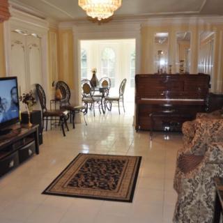A cozy living room features a piano, television, and elegant chandelier with a view into the dining area.