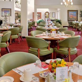 An elegant restaurant dining room with green chairs and beautifully set tables.