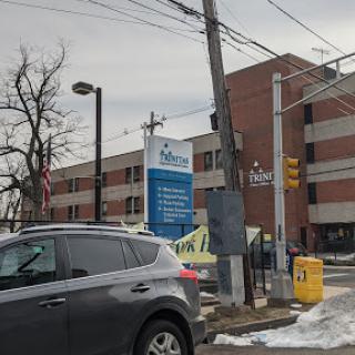A view of a hospital building with a prominent sign, surrounded by snow and parked vehicles on a winter day.