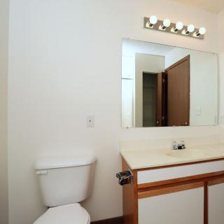 A clean and simple bathroom with a toilet, vanity, and mirror under a row of lights.