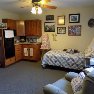 A cozy studio apartment with a small kitchen area, single bed, and comfortable seating.