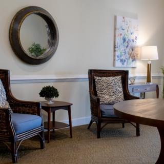 A cozy living room area with wicker chairs, a round mirror, and tasteful decor.