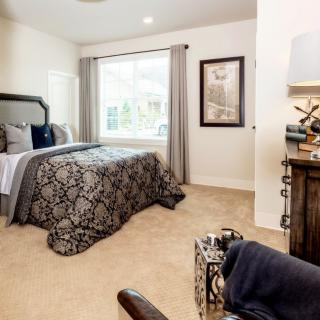 A cozy and elegantly decorated bedroom with patterned bedding, a large window, and stylish furnishings.