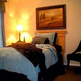 A cozy bedroom setting featuring a neatly made bed, a decorative painting on the wall, and a bedside lamp casting a warm glow.