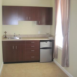 A compact kitchenette with wooden cabinets, a sink, small refrigerator, and curtains.