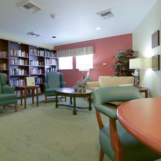 A cozy library room with chairs, tables, and bookshelves filled with books.