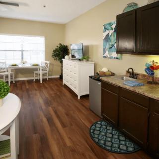 A cozy kitchen and dining area with hardwood floors, featuring dark cabinets, a small table with chairs, and a window letting in natural light.