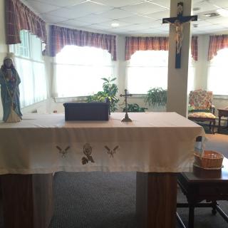A religious altar setup inside a small chapel, featuring a cross and a statue.