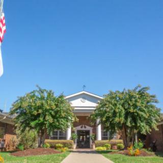 A well-maintained building entrance with greenery and a flag under a clear blue sky.