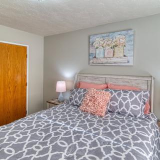 A cozy bedroom with a neatly made bed featuring patterned bedding, a bedside lamp, and artwork on the wall.