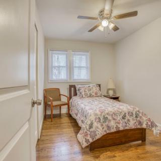 A cozy bedroom featuring a bed with floral bedding, a wooden chair, and a ceiling fan.