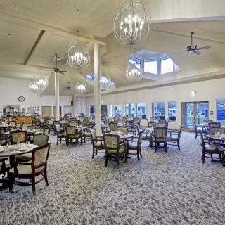 A spacious dining room with elegantly arranged tables and chairs, featuring chandeliers and large windows.