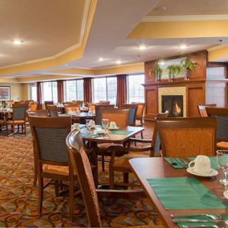 A spacious dining area with neatly arranged tables and chairs, featuring a warm fireplace and large windows.