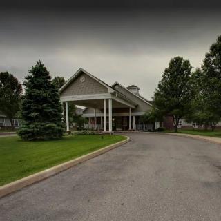 A view of a building with a driveway and surrounding trees under an overcast sky.