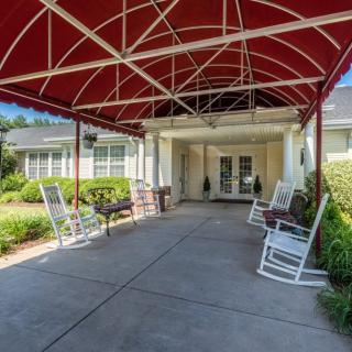 A building entrance with a red canopy and rocking chairs along the walkway.