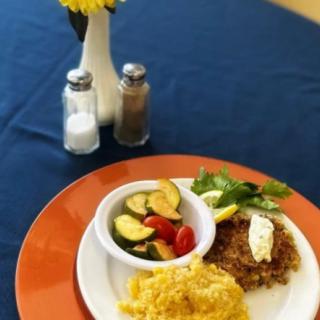 A breakfast plate featuring scrambled eggs, hash browns, and a side of zucchini and tomato salad is elegantly set on a table with salt, pepper, and a small vase with yellow flowers.