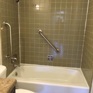 A bathroom featuring a bathtub with a handrail and tiled walls.