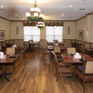 A cozy dining room with wooden floors, multiple tables and chairs, and elegant chandeliers.