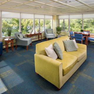 A bright lounge area featuring a yellow sofa, various chairs, and large windows letting in natural light.