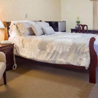 A cozy bedroom with a neatly made bed, nightstand, and comfortable chair.
