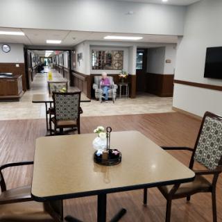A cozy common area in a healthcare facility featuring tables, chairs, and a long corridor.