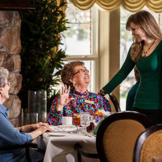 Three women engaged in conversation at a dining table indoors.