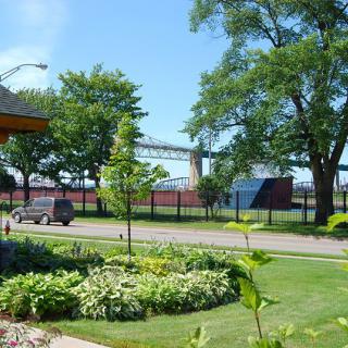 A scenic view of a bridge in the background with trees, a road, and well-maintained lawns in the foreground.
