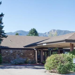 A building entrance surrounded by greenery with mountains in the background.