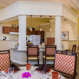 A cozy dining area with a kitchen in the background featuring elegant chairs and a well-set table.