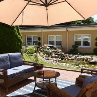 A cozy patio area with wooden furniture and a large umbrella, overlooking a landscaped garden.