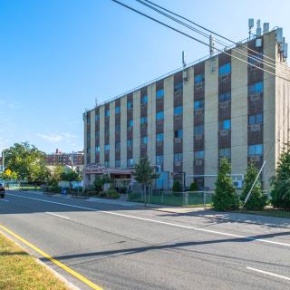 A residential apartment building located beside a quiet urban street under a clear blue sky.