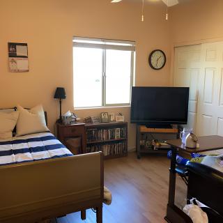 A cozy bedroom with a bed, television, and bookshelf by the window.