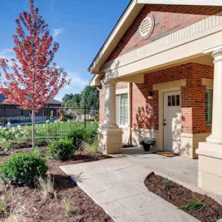 A charming building with a welcoming entrance, surrounded by landscaped gardens and vibrant trees.