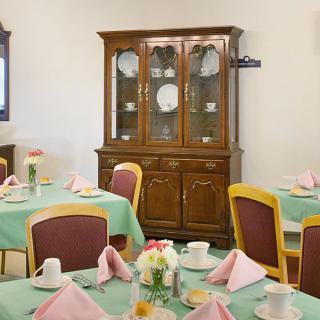 A neatly arranged dining room featuring tables with teal tablecloths, pink napkins, and a wooden china cabinet in the background.