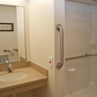 A modern bathroom with a sink, mirror, and accessible shower.