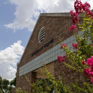 A brick building with a sign reading 'Student Center', surrounded by blooming pink flowers under a cloudy sky.