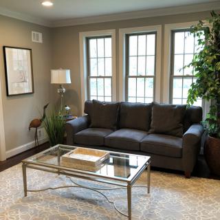 A modern living room featuring a dark gray sofa, a glass coffee table, and large windows with natural light.