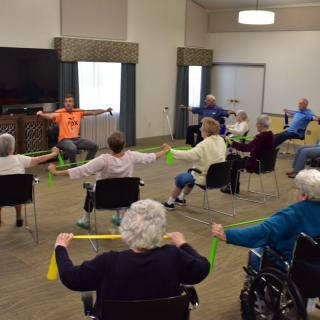 A group of elderly individuals participating in a fitness class using resistance bands at a community center.
