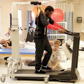 A patient undergoing physical therapy with assistance on a specialized treadmill.